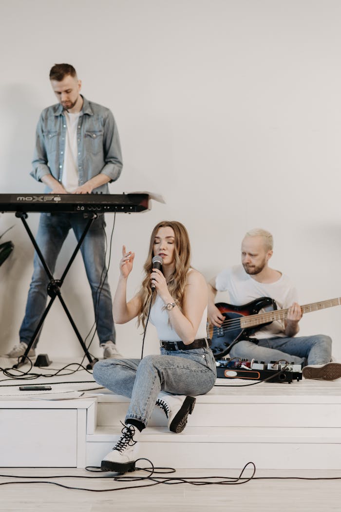 Three musicians rehearsing indoors with a keyboard, guitar, and microphone.