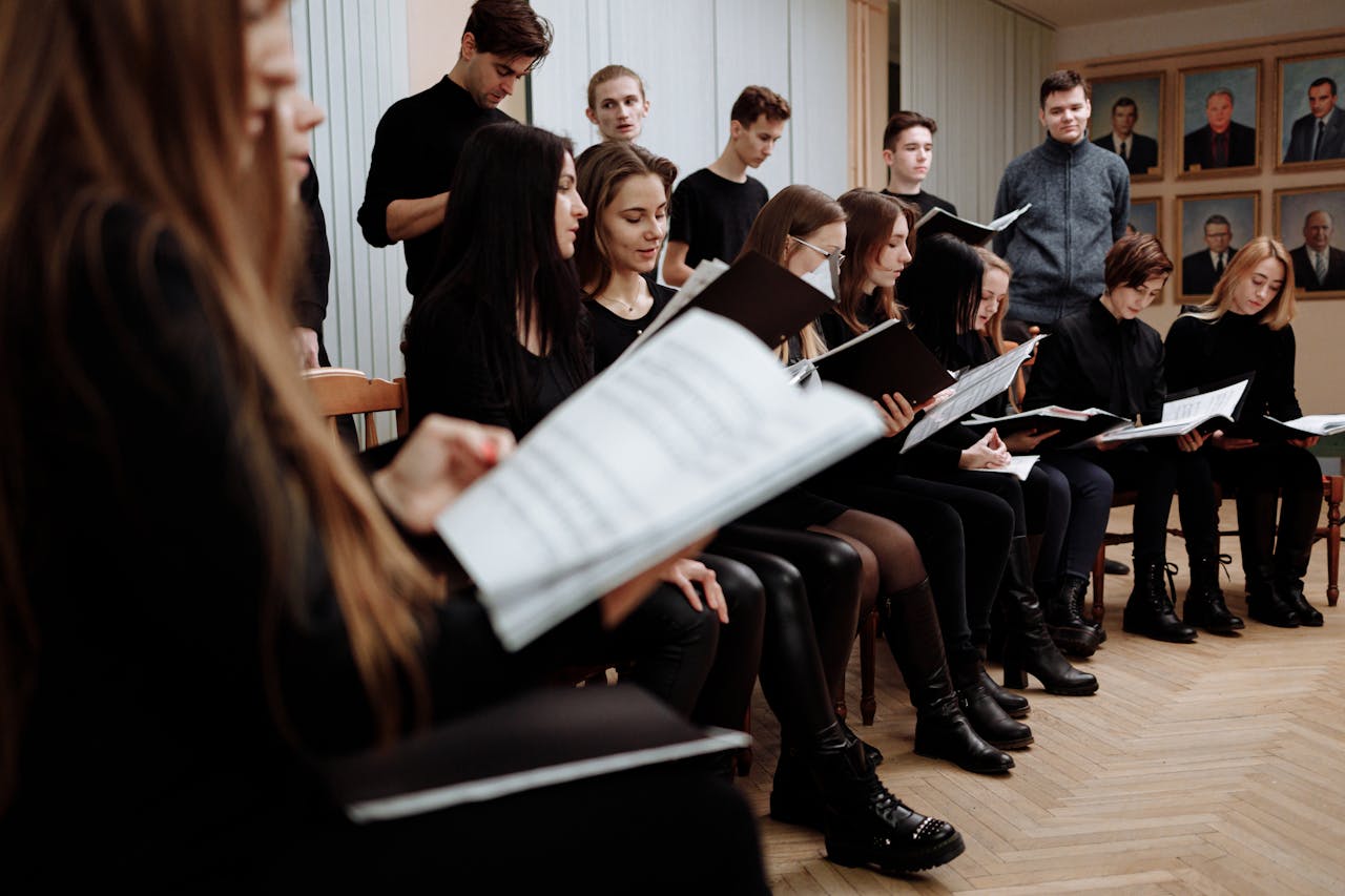 A choir rehearses indoors, focusing on music sheets for performance practice.