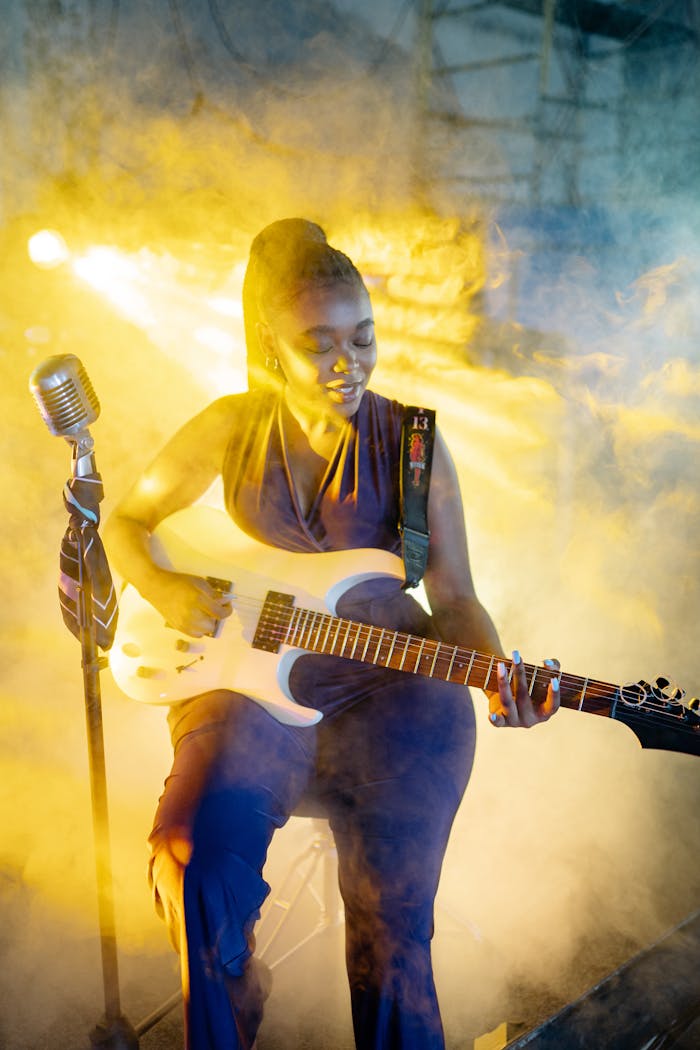 An engaging performance with a female guitarist enveloped in vibrant stage lights and smoke.